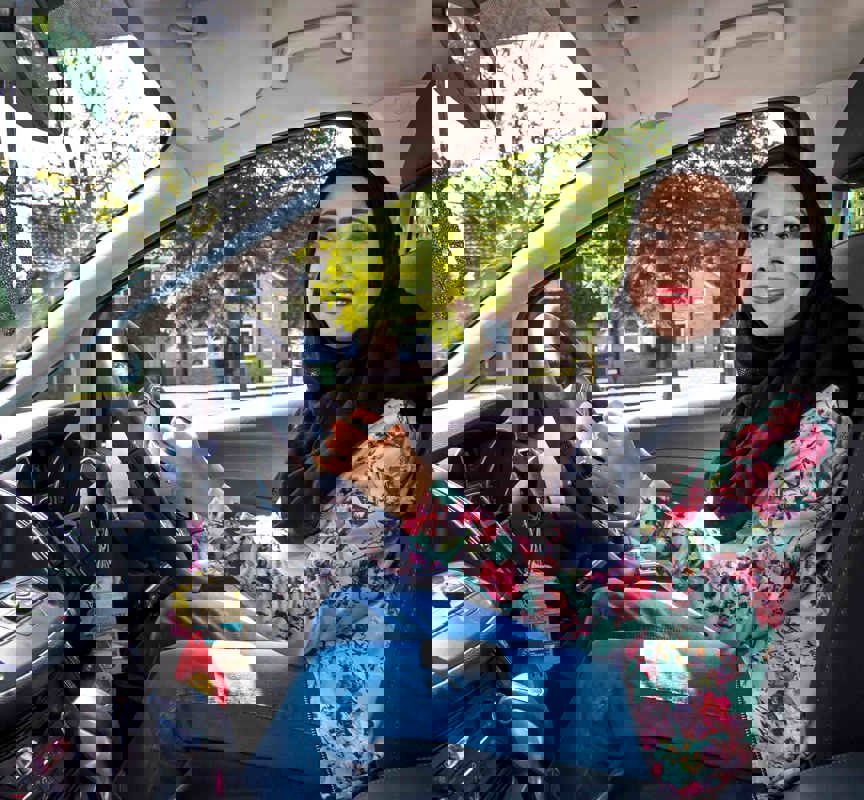 Nazmin is sat in the driving seat of her car with her hands on the specially adapted steering wheel